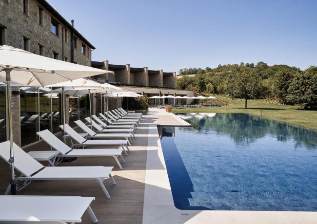 Outdoor pool with white loungers and umbrellas near a stone building.