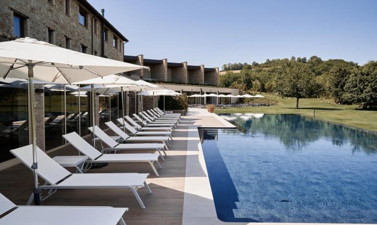 Piscine extérieure avec chaises longues blanches et parasols près d'un bâtiment en pierre.