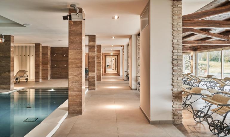 Indoor pool with loungers, columns, and large windows.